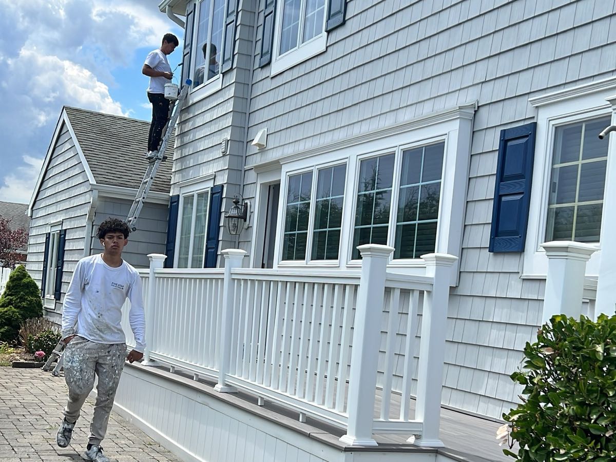 Equipo de Prime Paint pintando el exterior de una casa con barandas blancas y persianas azul marino