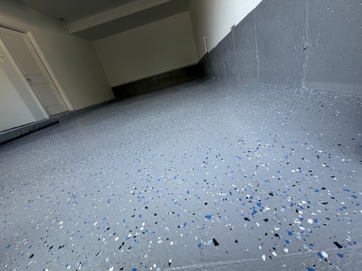Piso de garaje terminado con revestimiento epóxico gris y hojuelas decorativas azules, blancas y negras