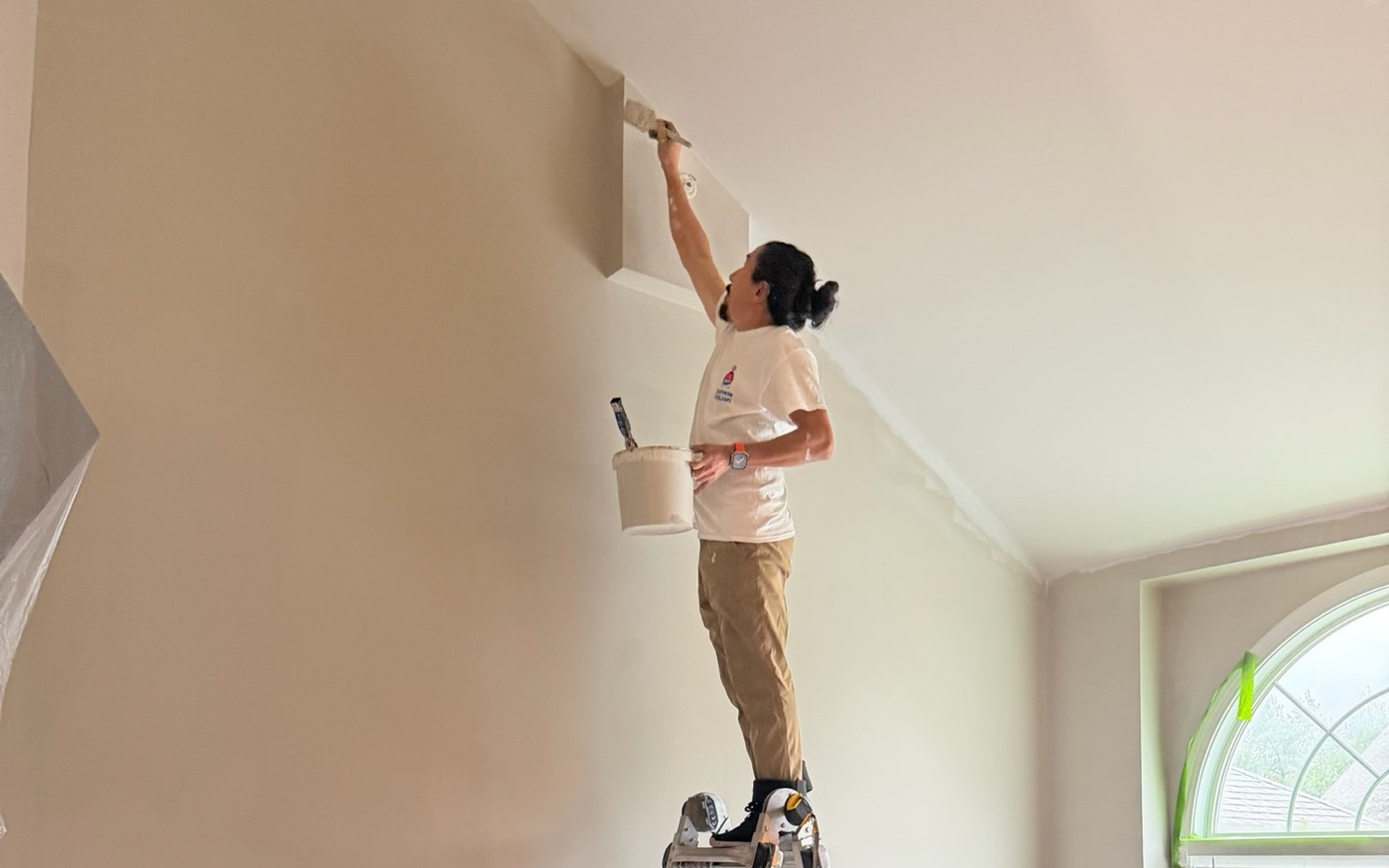 Pintor de Prime Paint en una escalera cortando la l&iacute;nea del techo con el cuarto cubierto