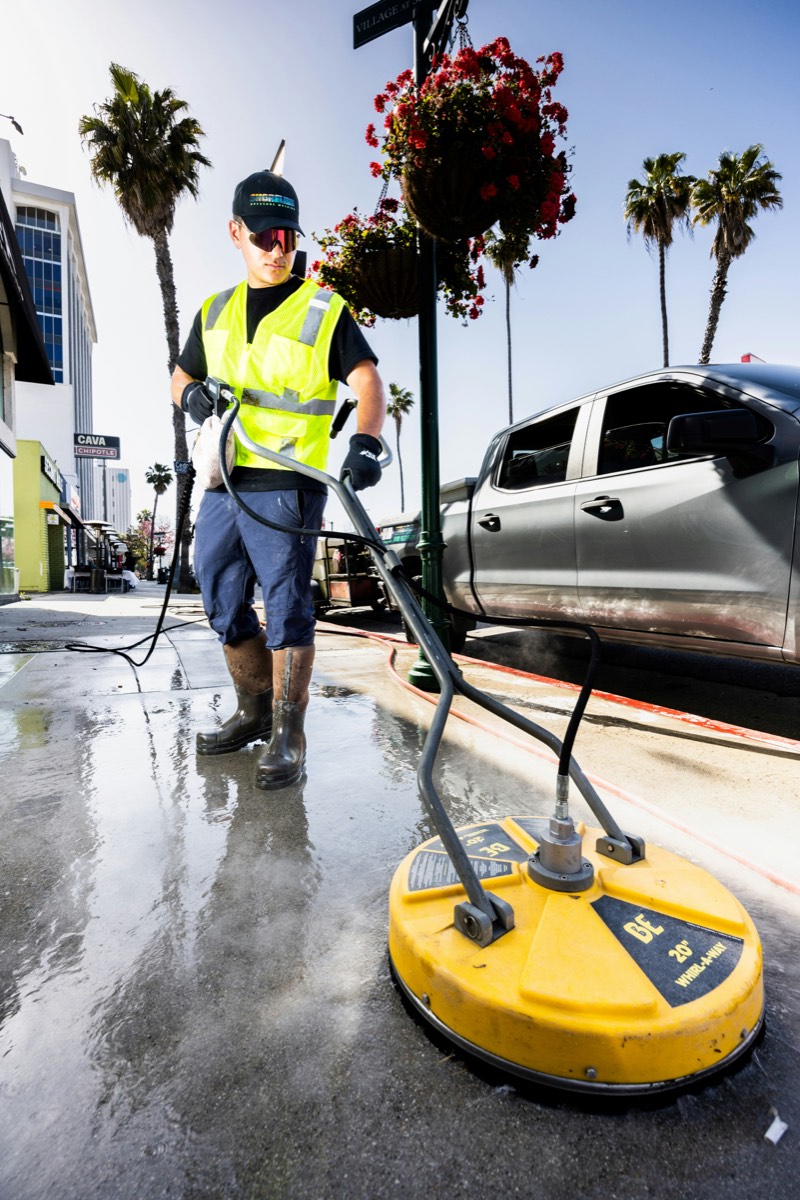 Worker cleaning a concrete walkway with a surface-cleaner pressure washer