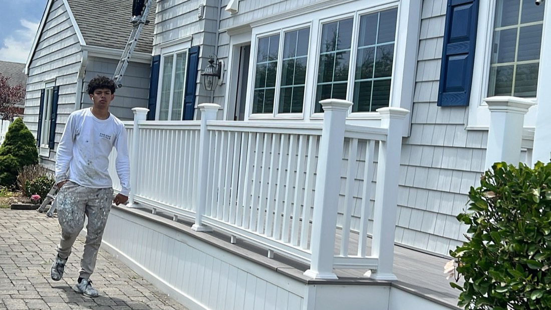Crew working on the white siding and porch railings of a two-storey home